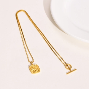 Close-up of golden stainless steel necklace with square relief pendant and toggle clasp