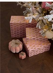 Close-up of pink gift boxes with gold bows and velvet pumpkins by a Christmas tree