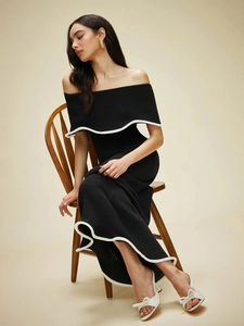 Elegant off-shoulder black knit maxi dress with white trim on a wooden chair