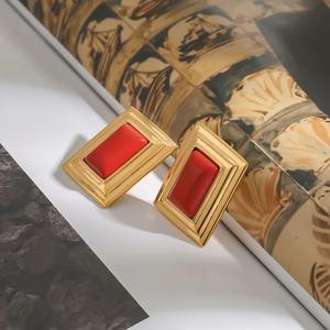 Detailed view of vintage rectangular gold earrings with vibrant red inserts on stone background