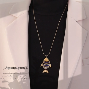 Detailed close-up of golden fish pendant with blue enamel on a black sweater base