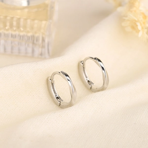 Minimalist silver Mobius twist hoop earrings on elegant beige linen fabric backdrop