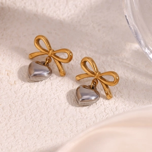 Détail de boucles d'oreilles nœud plaqué or 18K avec pendentif cœur argenté sur blanc