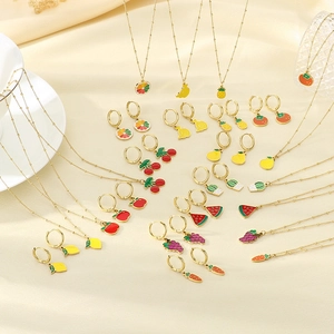 Détail de la collection de bijoux fruités en émail sur fond en tissu beige doux