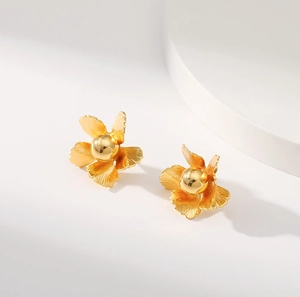Macro detail of golden flower earrings featuring textured petals and a smooth center bead