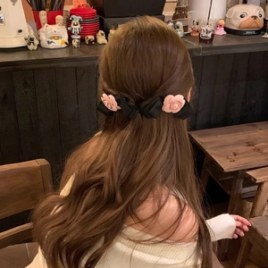 Close-up of black satin bow hair clips with pink rose detail worn on a half-up hairstyle