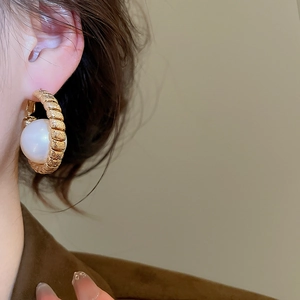 Detailed view of elegant gold hoop earrings with spiral texture and large white pearls
