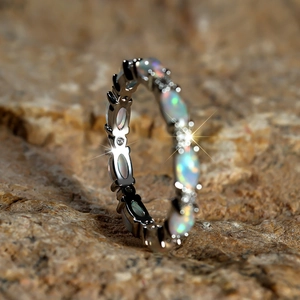 Detail of oval-cut opal eternity ring with vibrant fire effect on a natural rock background