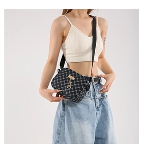 Detail shot of a black monogram crossbody bag with gold deer charm on a white vest model