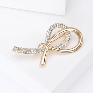 Elegant gold ribbon knot brooch with clear rhinestones on white geometric background