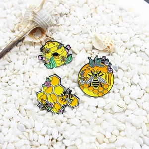 Drei detaillierte Emaille-Pins mit Bienen und Waben auf Naturstein und Muscheln