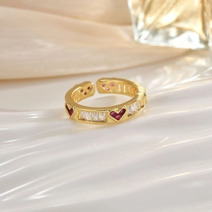 Detail of gold open ring featuring a red heart-shaped gem and baguette crystals
