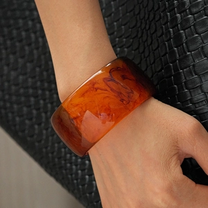 Macro detail of wide amber resin bangle showing natural smoky texture and mirror finish