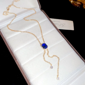 Detailed macro view of a gold Y-shaped necklace with a square blue gemstone and tassels