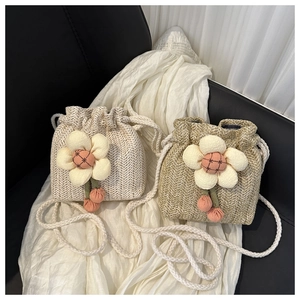 Dettaglio di mini borse a secchiello in paglia con fiori e tracolle a cordoncino