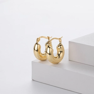 Detail of s925 sterling silver gold plated hoop earrings on white stone pedestal