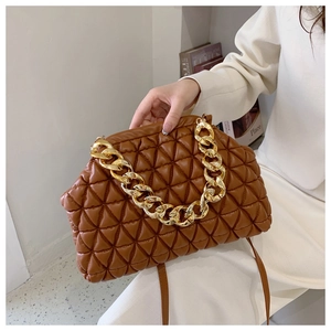 Detail of brown quilted shoulder bag with chunky gold chain strap held by a model