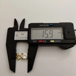 Digital caliper measuring the 15.9mm width of a gold elk pendant with white zircon