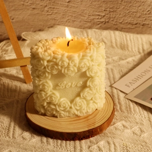 Detail of white cylindrical rose candle with embossed Love lettering on a wood base