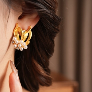 Close-up of vintage gold earrings with white pearls and crystals on a female model