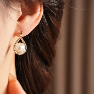 Close-up of a French vintage gold drop earring with a central pearl on a model's ear