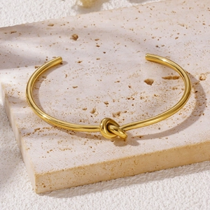 Elegant gold-plated stainless steel knot cuff bracelet on a minimalist stone background