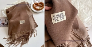 Detailed view of brown cashmere-style scarf featuring fringe edges and woven brand label