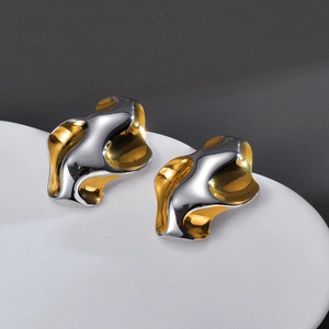 Detail shot of wavy gold and silver mixed metal earrings on a white ceramic plate