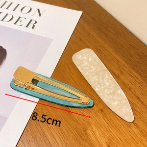 Detail shot of 8.5cm vintage acetate hair clips in teal and cream on a wooden desk