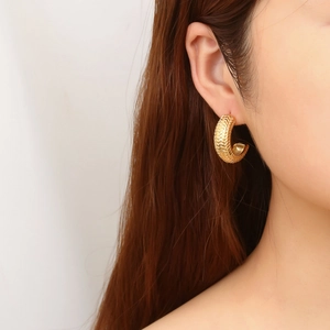 Detailed view of gold C-shaped earrings with wheat-ear texture on female model