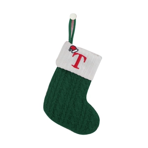 Close-up of green knitted Christmas stocking with white cuff and red embroidered letter T