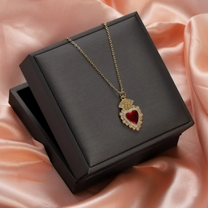 Close-up of red heart ruby pendant on golden chain resting on a black gift box