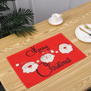 Close-up view of a red linen Christmas placemat with Santa Claus motifs and Merry Christmas text