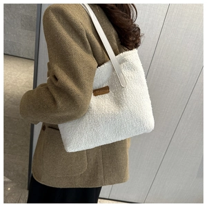 Close-up of white plush tote bag with FASHION leather tag on woman's shoulder