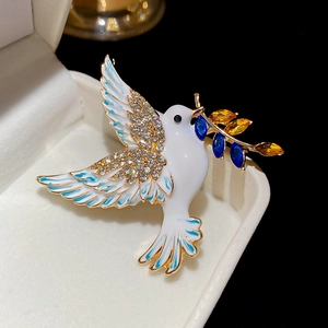 Close-up of peace dove brooch with white enamel, rhinestones, and blue olive branch