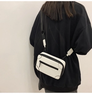 White leather crossbody bag with black zippers shown on model in a minimalist style