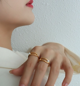 Close-up of a gold-plated geometric ring featuring a pearl detail on a model's finger