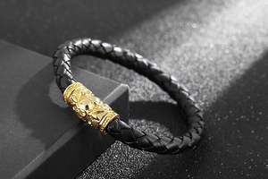 Detail of black woven leather bracelet with golden engraved stainless steel tube accents