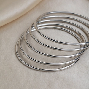Detail of five interlocking silver stainless steel bangles on elegant silk fabric