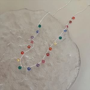 Close-up of a silver beaded necklace with colorful faceted gemstones on a frosted tray