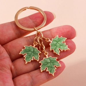 Close-up of golden keychain with three green gingko leaf pendants in enamel finish
