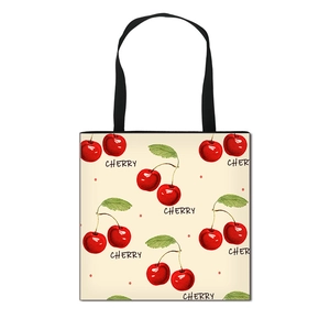 Foldable canvas shopping bag with red cherry print and black handles on cream background