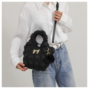 Detail of black pleated cloud bag with gold bow ornament and fuzzy pompom accessory