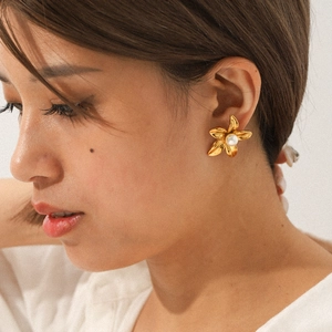 Detailed view of 18k gold plated flower earring with pearl center worn by a model
