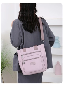 Rear view of a pink oxford crossbody bag with adjustable strap worn on a gray blazer