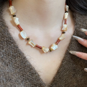 Detail of ethnic style necklace with irregular white shell and reddish beads on a model