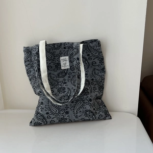 Detailed close-up of grey paisley canvas tote bag with white straps and fabric label