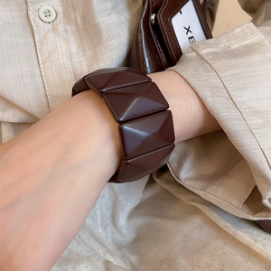 Detail of a dark brown wide geometric bangle with pyramid pattern and polished finish