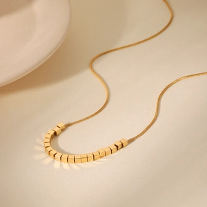 Gros plan d'un collier chaîne serpent dorée avec perles cubiques sur une surface mate