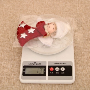 Detail view of a red felt angel ornament with white feather wings weighing 13g on a scale